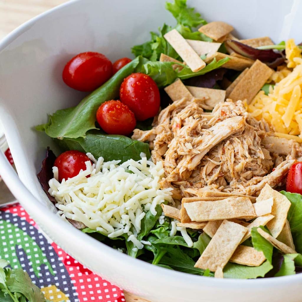 Copycat Cafe Rio Chicken on a bed of salad greens with toppings in a white bowl.