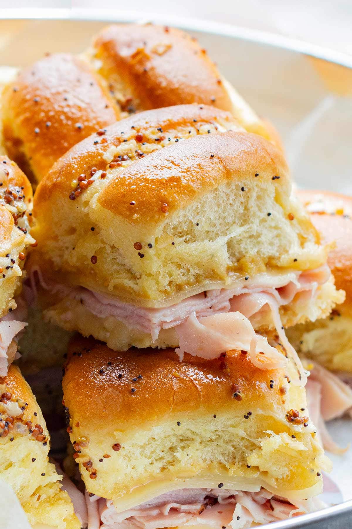 Close up shot of make-ahead ham & cheese hawaiian sliders stacked on a tray.