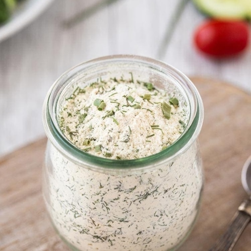 Powdered dry ranch seasoning mix in a small glass jar on a cutting board.