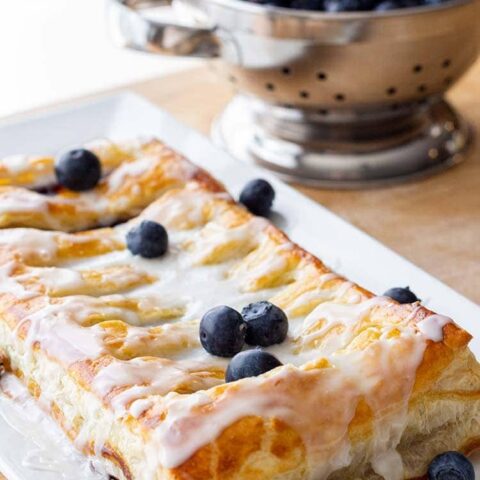 Make-Ahead Blueberry Cream Cheese Danish on a platter, with a collander of fresh blueberries in the background.