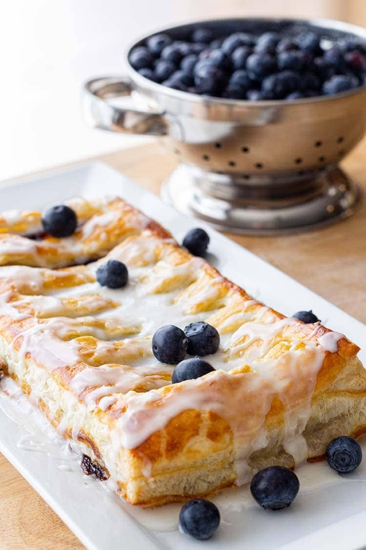 Make-Ahead Blueberry Cream Cheese Danish on a platter, with a collander of fresh blueberries in the background.