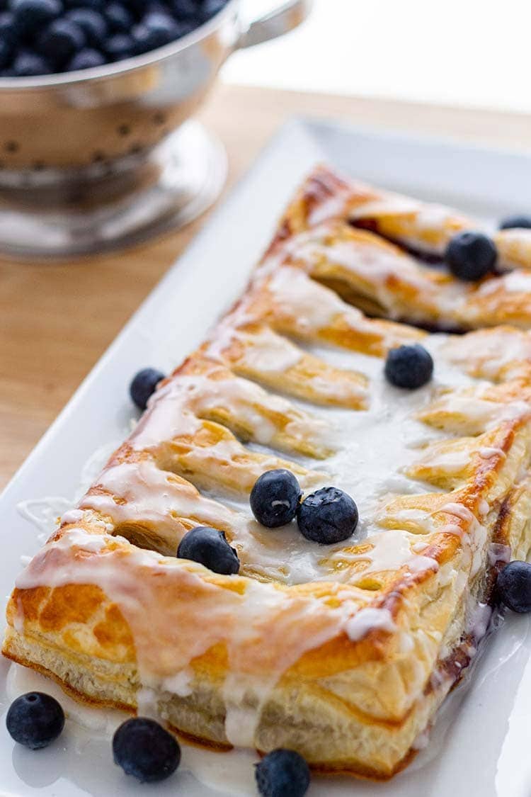 Make-Ahead Blueberry Cream Cheese Danish on a white plate, with icing and fresh blueberries.