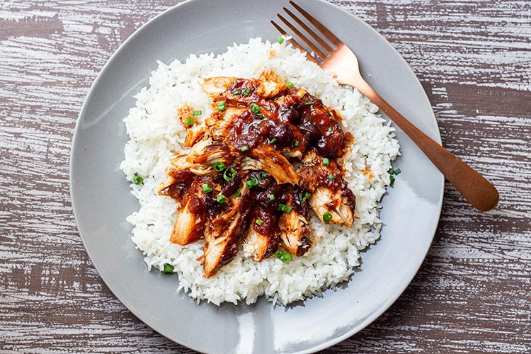 Cranberry Catalina Chicken served on a bed of white rice atop a gray plate sitting on a gray board background.