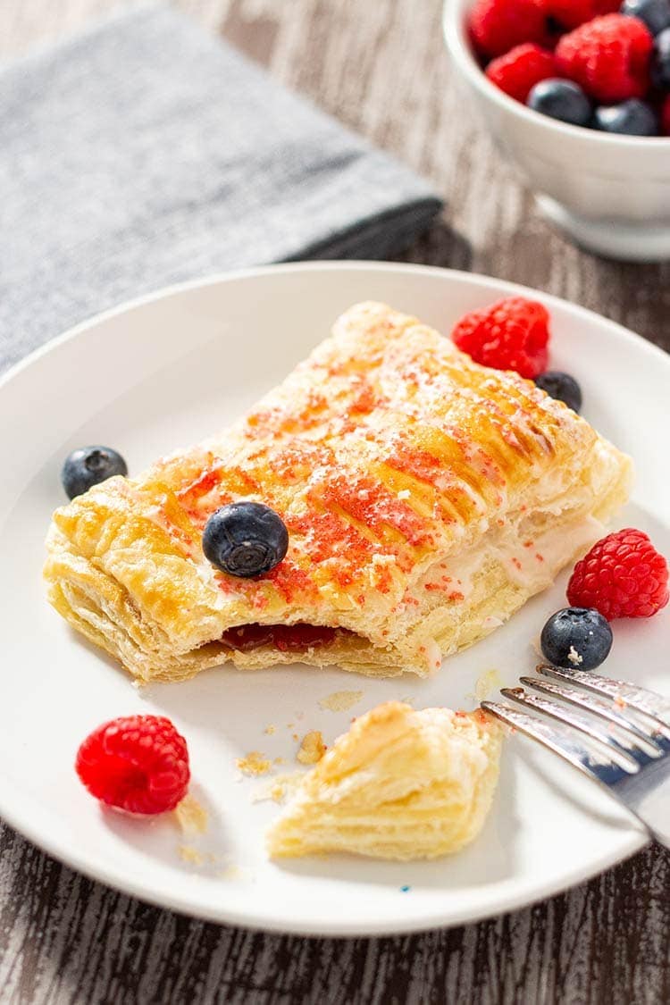 Raspberry Easy Breakfast Pastry on a white plate on a wooden tray, with corner cut open to show jam inside.