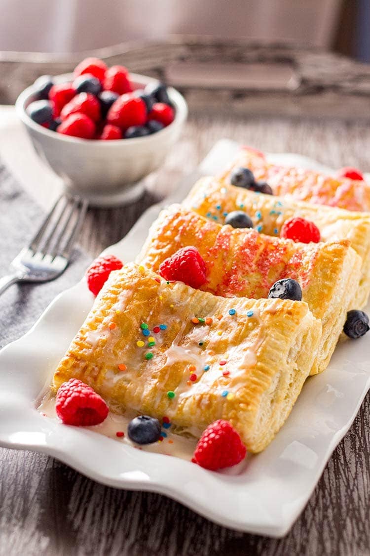 Easy Breakfast Pastries laid out on white rectangular plate on wooden tray with bowl of raspberries and blueberries in background.