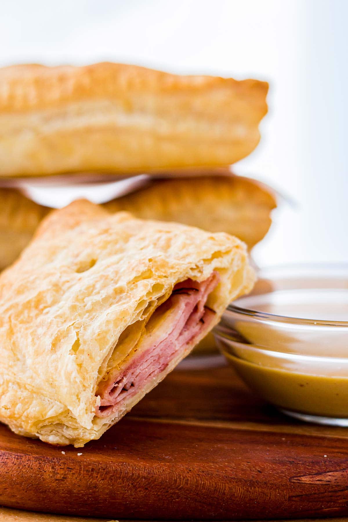 Closeup of homemade ham & cheese hot pocket with puff pastry and mustard dipping sauce on side.