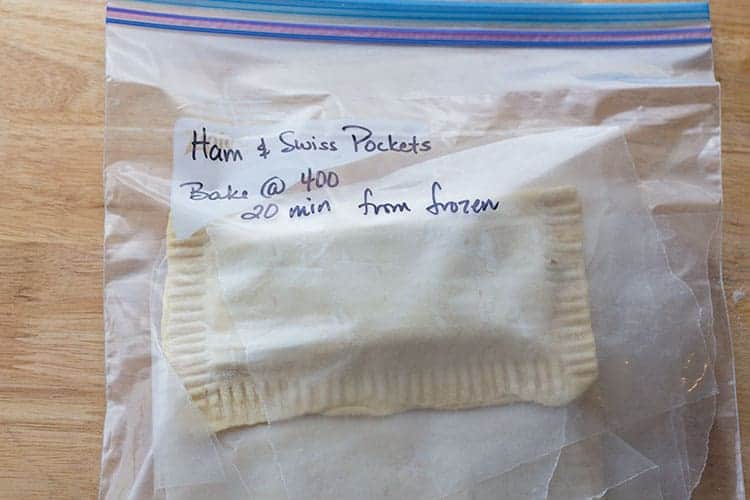 Gallon zip top bag containing frozen homemade ham and cheese hot pocket with instructions written in sharpie on bag.