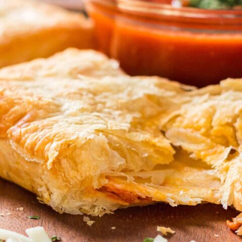 Puff pastry pizza pocket on tray with dipping sauce in background.