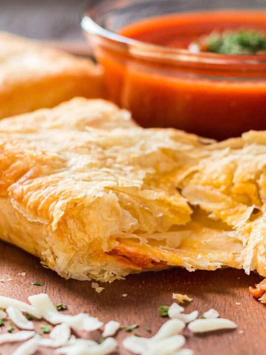 Puff pastry pizza pocket on tray with dipping sauce in background.