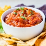 Closeup of freezer salsa prepared and in a white dish for serving, garnished with chopped cilantro and surrounded by tortilla chips.