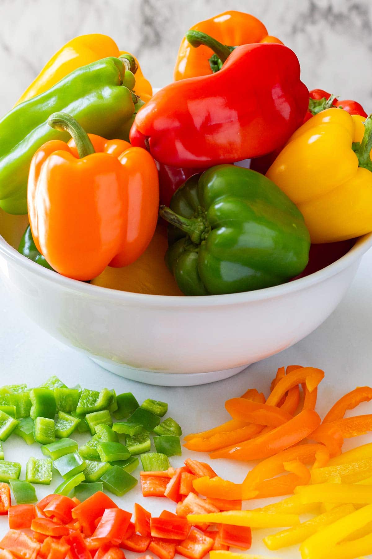Bowl of bell peppers with sliced and diced bell peppers on counter in front.
