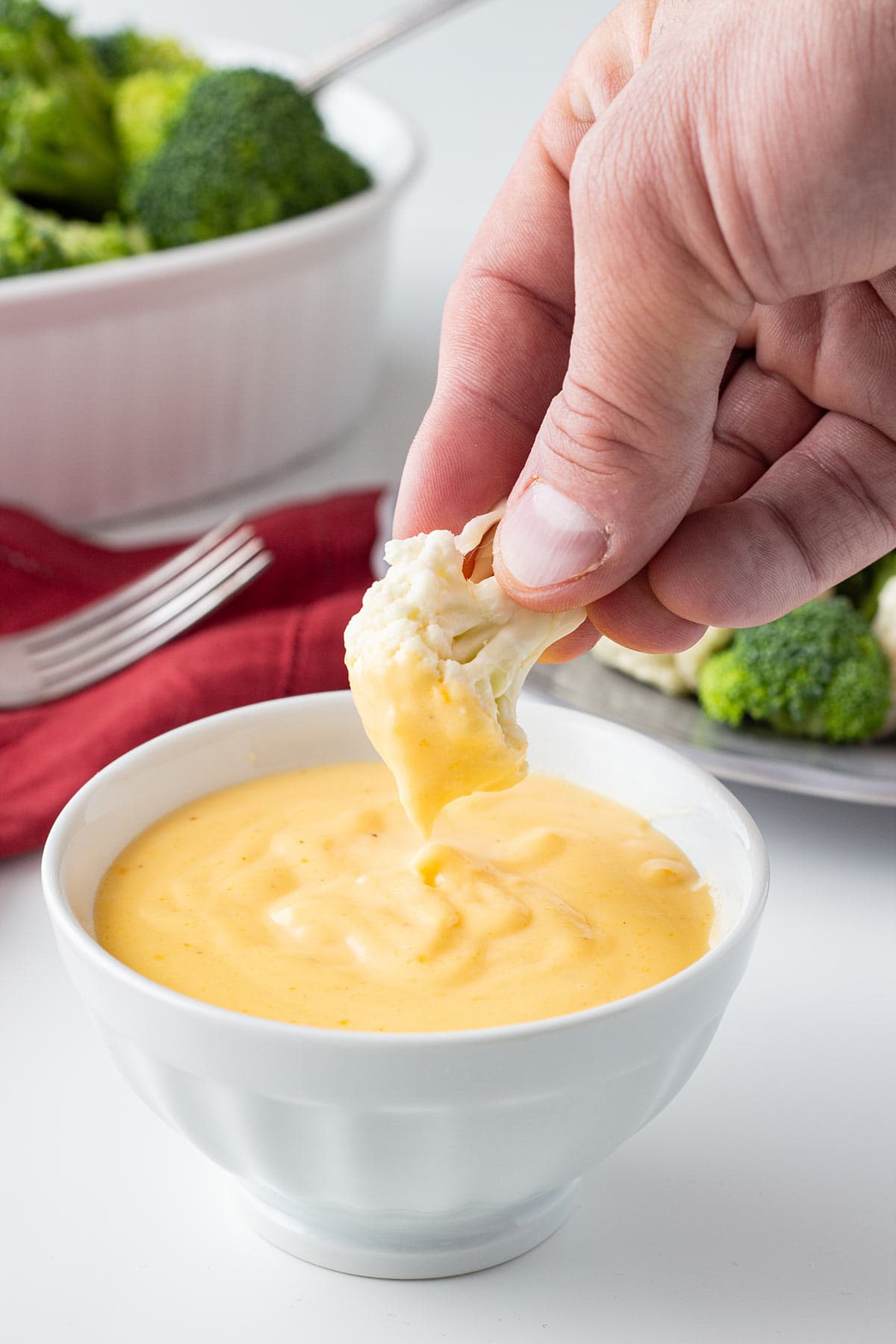 Cauliflower being dipped into a bowl of Freezable Cheese Sauce.