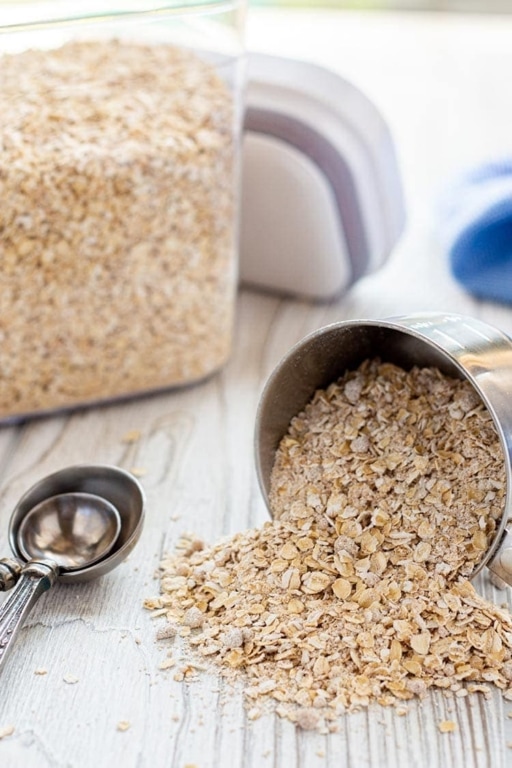 Homemade instant oatmeal mix spilling out of mixing cup onto countertop.