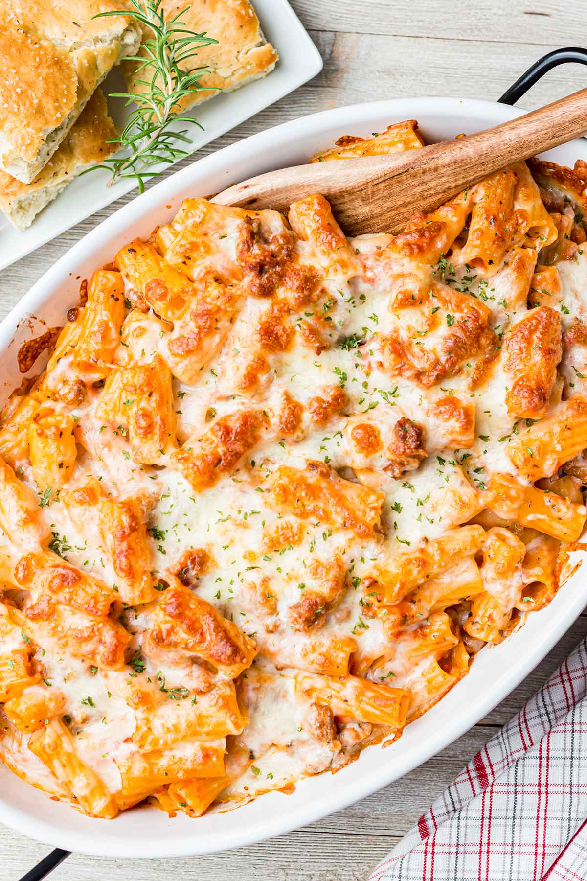 Overhead shot of baked Sausage Cheese Rigatoni in a white oval baking dish with side of foccacia bread.