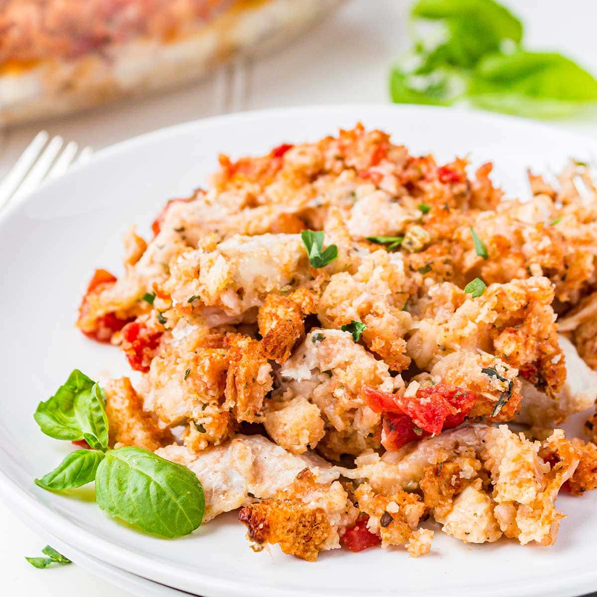 Closeup shot of Bruschetta Chicken Bake dished on white plate and garnished with fresh basil.