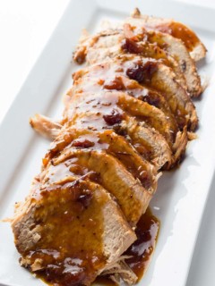 Spiced Cranberry Pork Roast sliced on a platter and covered with pan juice gravy