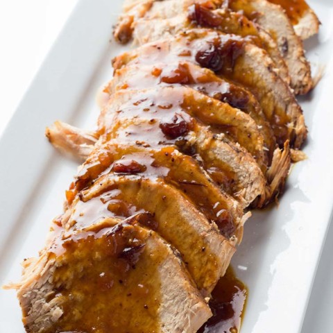 Spiced Cranberry Pork Roast sliced on a platter and covered with pan juice gravy