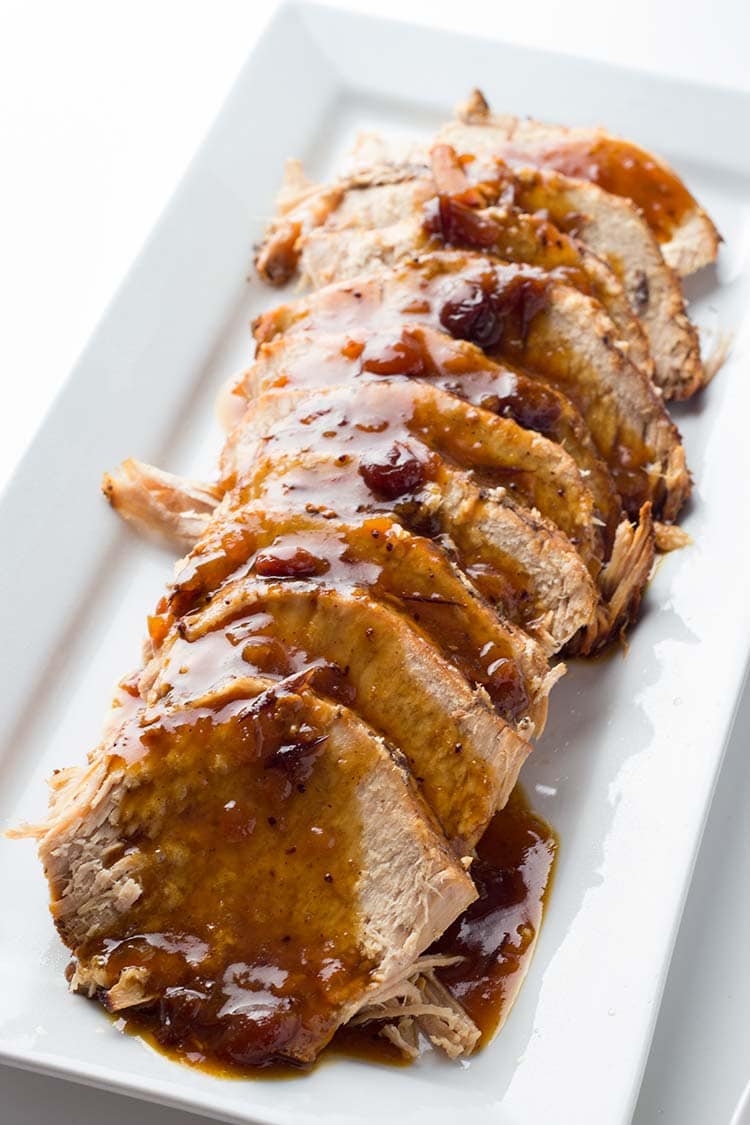 Spiced Cranberry Pork Roast sliced on a platter and covered with pan juice gravy