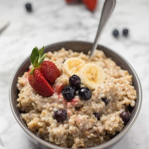 Bowl of steel cut oatmeal on marble background with cut fresh fruit