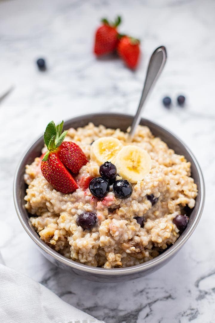 Bowl of Instant Pot Easy Steel Cut Oatmeal on marble countertop garnished with fresh strawberries, blueberries and sliced banana.