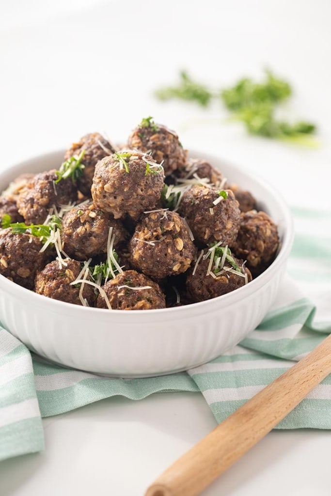 Easy Baked Freezer Meatballs piled in a white bowl and garnished with chopped parsley and Parmesan cheese.
