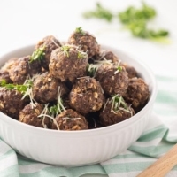 Easy Baked Freezer Meatballs piled in white bowl and garnished with parsley and Parmesan cheese.