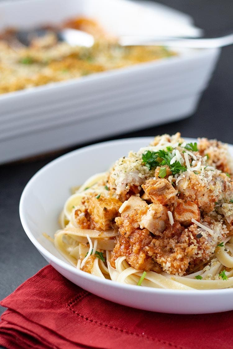 Easy Chicken Parmesan Casserole dished on a plate over linguine, garnished with shredded Parmesan cheese and fresh parsley