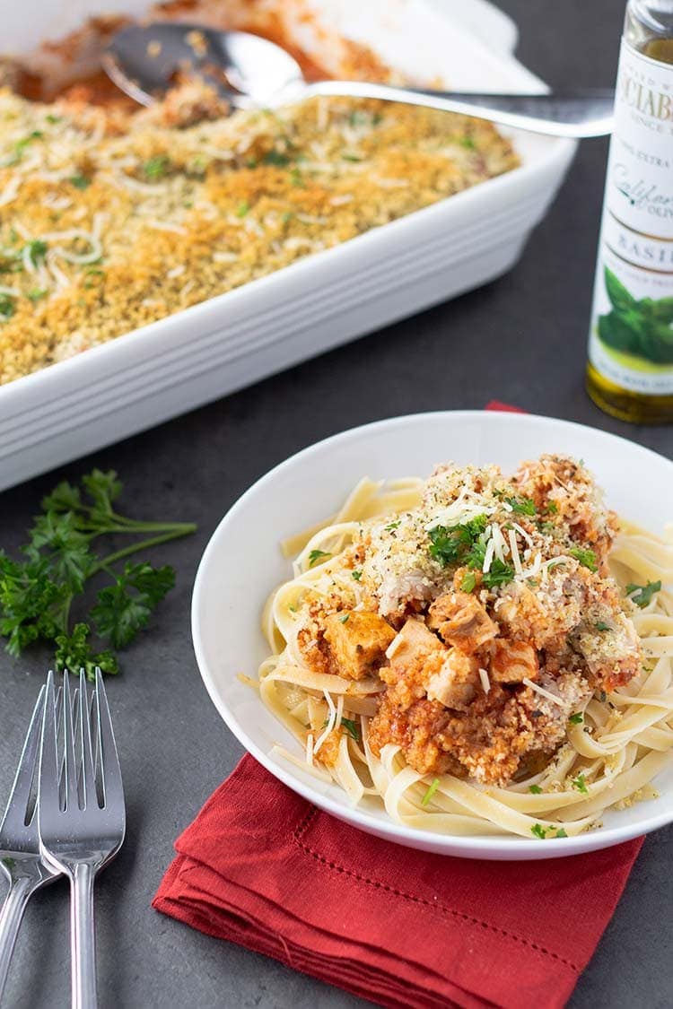 Baking dish of Easy Chicken Parmesan Bake and a serving dished onto a plate on top of linguine noodles ready to eat