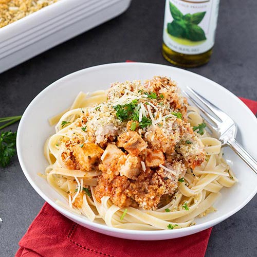 Easy Chicken Parmesan Bake served over linguine on white plate sitting atop a folded red fabric napkin