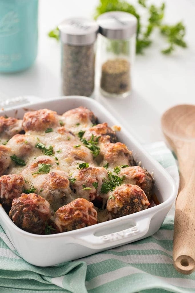 Easy Keto Meatballs in a white baking dish, covered with marinara sauce and topped with melted mozzarella cheese, garnished with fresh parsley