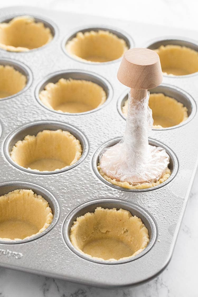 LowCarb Mini Quiches with Almond Flour Crust, with crust dough in the muffin tins demonstrating how to use the pastry tamper