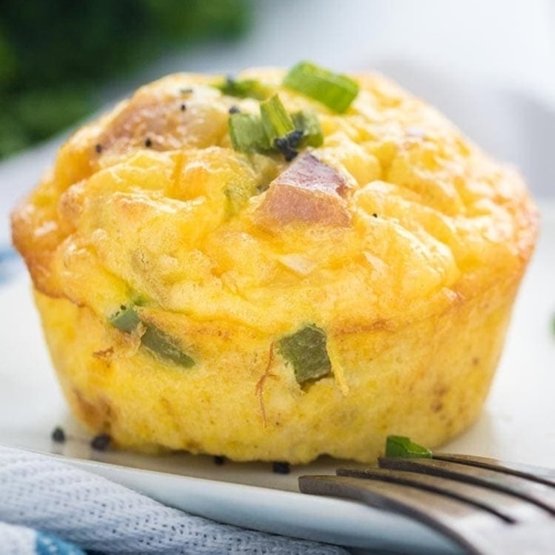 A Denver Omelet Egg Muffin on a white plate, garnished with sliced scallions and course sea salt.