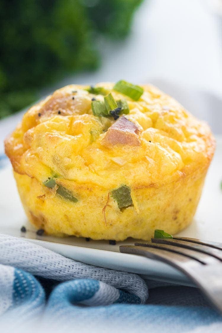 A Denver Omelet Egg Muffin on a white plate, garnished with sliced scallions and course sea salt.