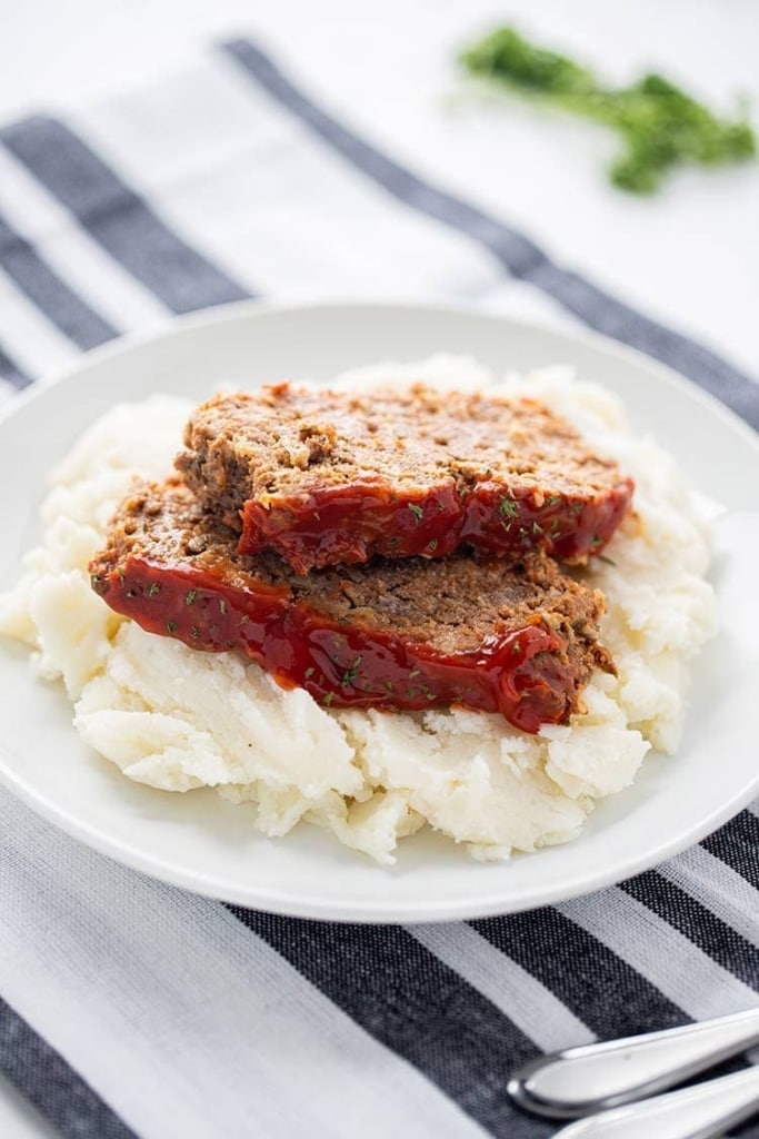 Two slices of Instant Pot Meatloaf set on top of a bed of mashed potatoes and garnished with chipped parsley.
