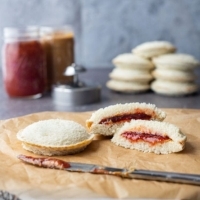 Homemade uncrustables sandwiches on a counter, with one cut open to show the peanut butter and jam inside.