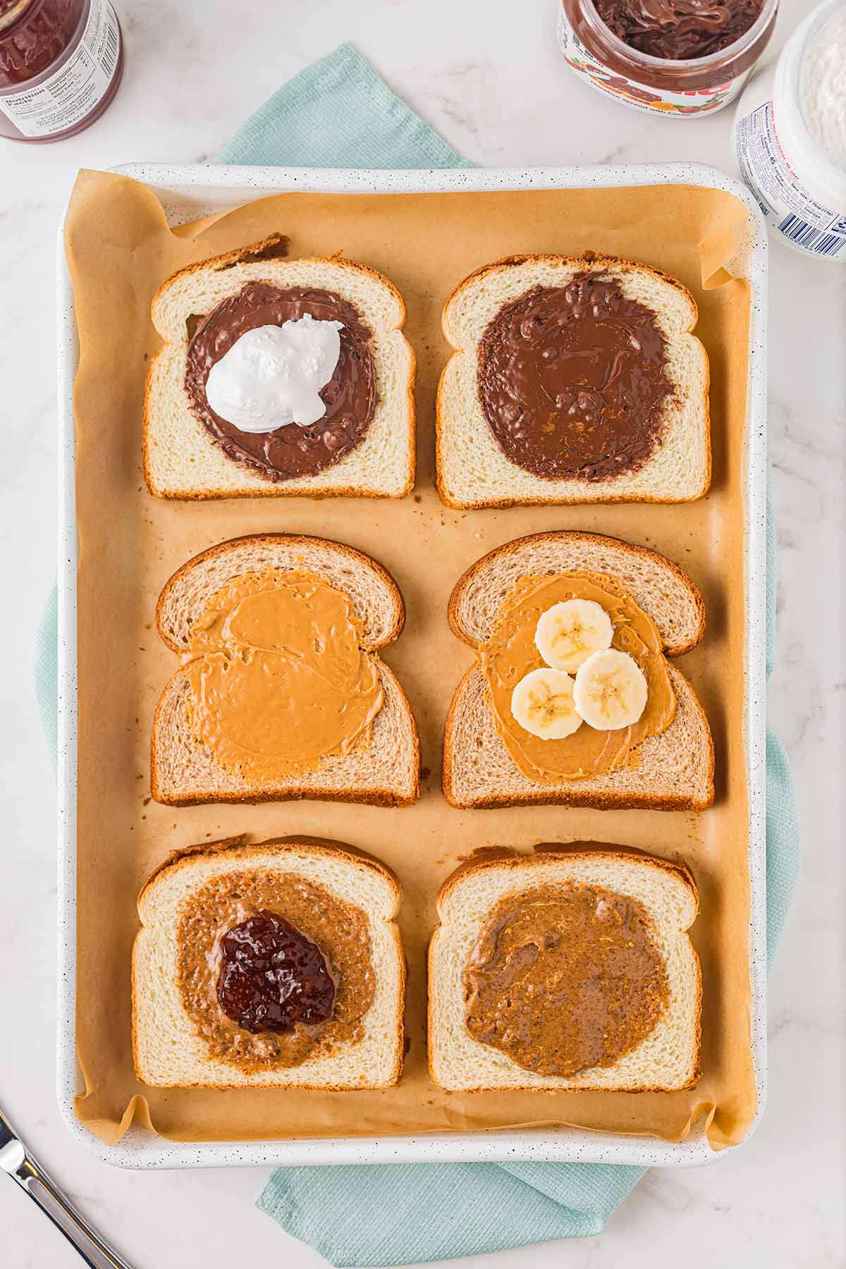 Overhead shot of different variations of fillings for homemade uncrustables sandwiches, including nutella and fluff, peanut butter and banana, and nut butter and grape jelly.