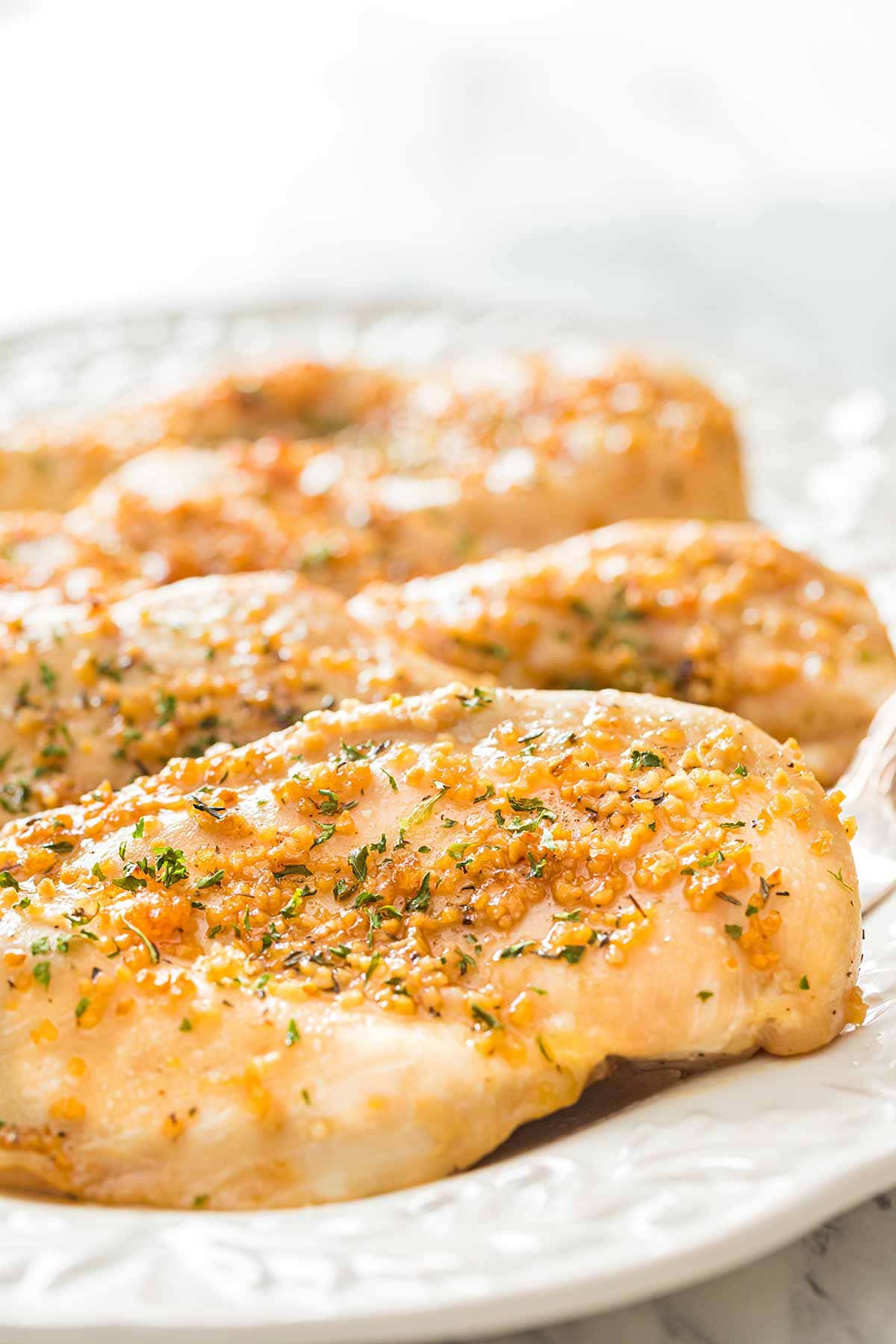 Closeup shot of baked Garlic Brown Sugar Chicken breasts arranged on white serving platter.