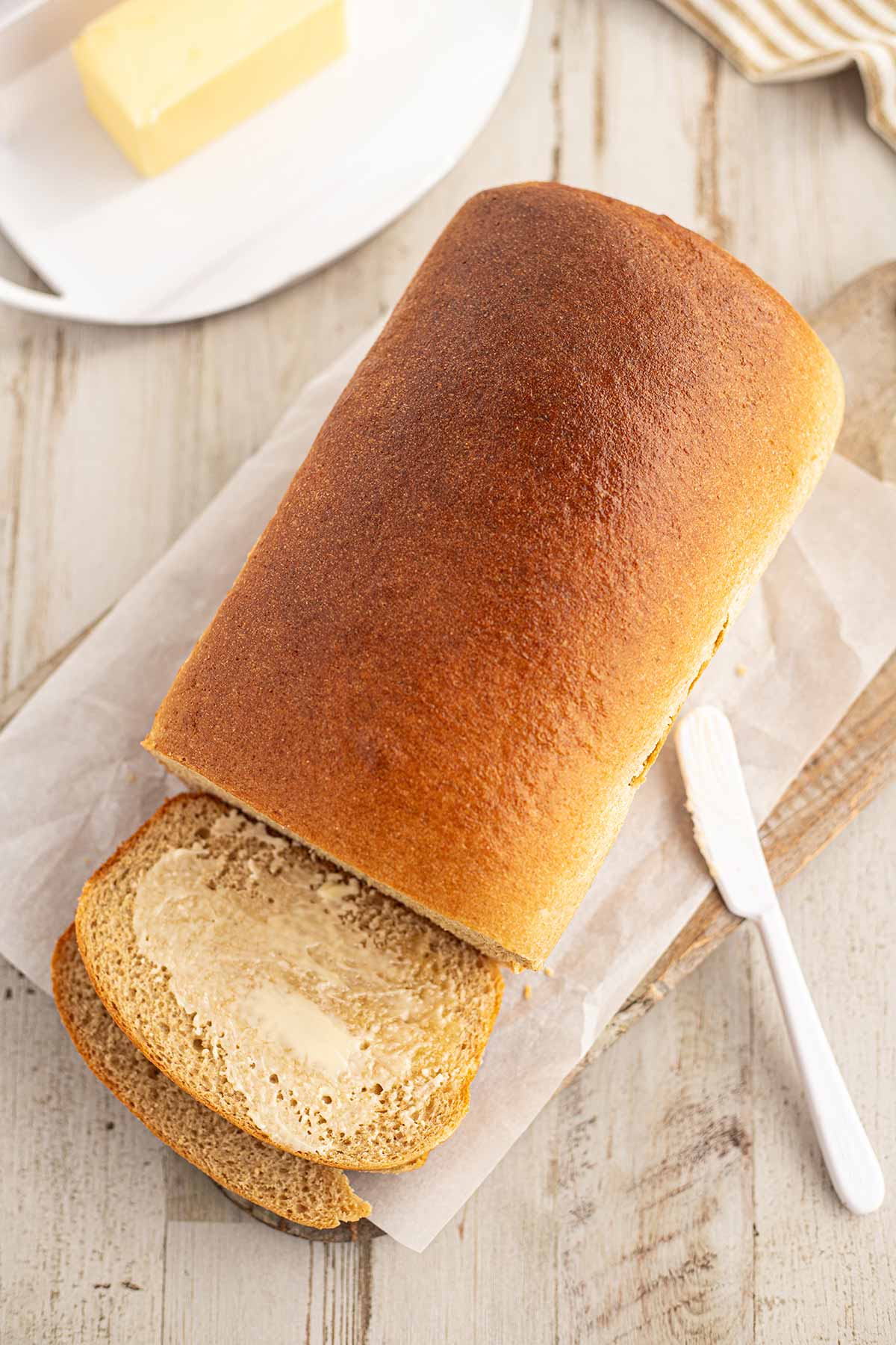 Overhead shot of loaf of honey wheat bread on counter, with butter and knife.