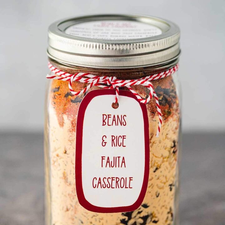 Mason jar, on gray background, filled with the dry ingredients used to make Bean & Rice Fajita Casserole, sealed and a printed label tied to the rim of the jar.