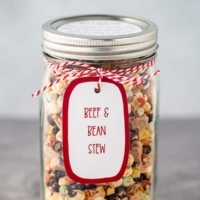 Quart mason jar on gray background, filled with the dry ingredients for making Beef & Bean Stew, with a printed label tied to the jar.