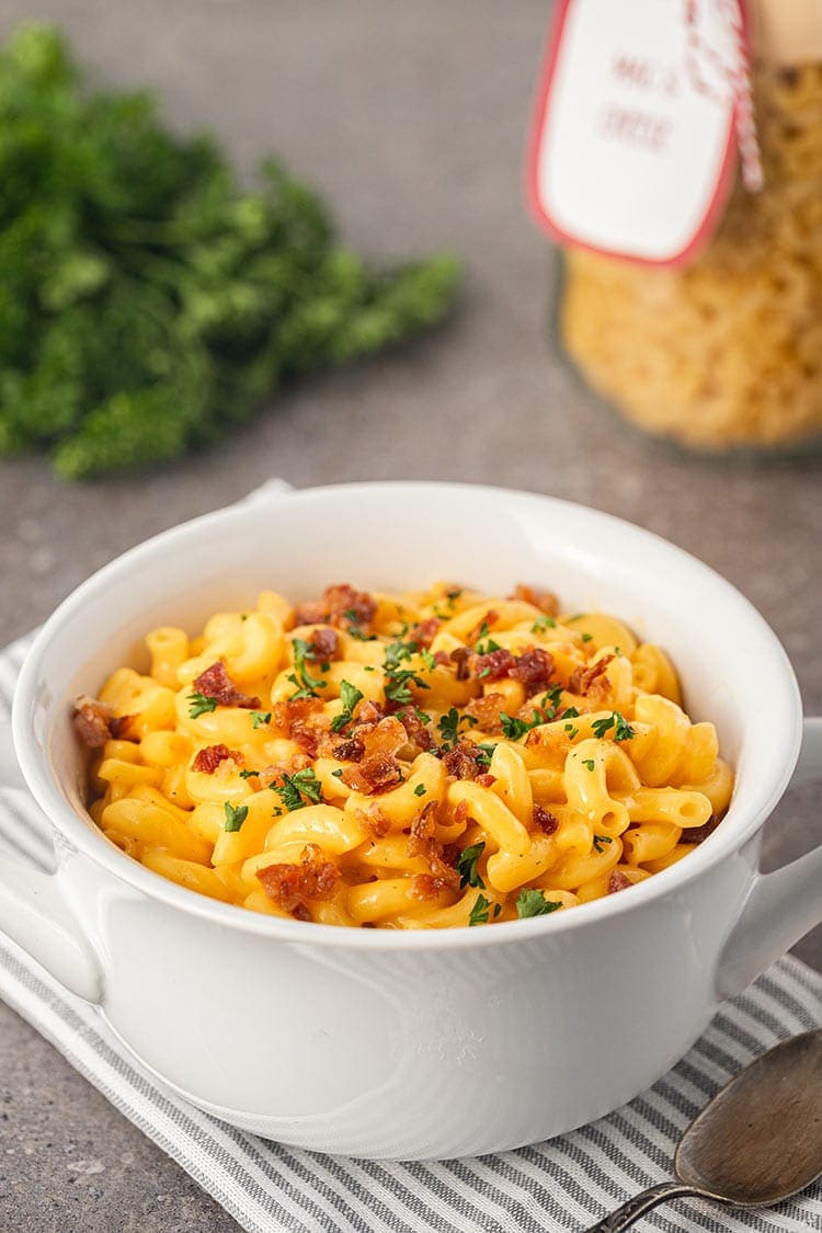 Mac & Cheese Meal in a Jar made into a meal, in a white bowl, topped with bacon crumbles and fresh parsley.