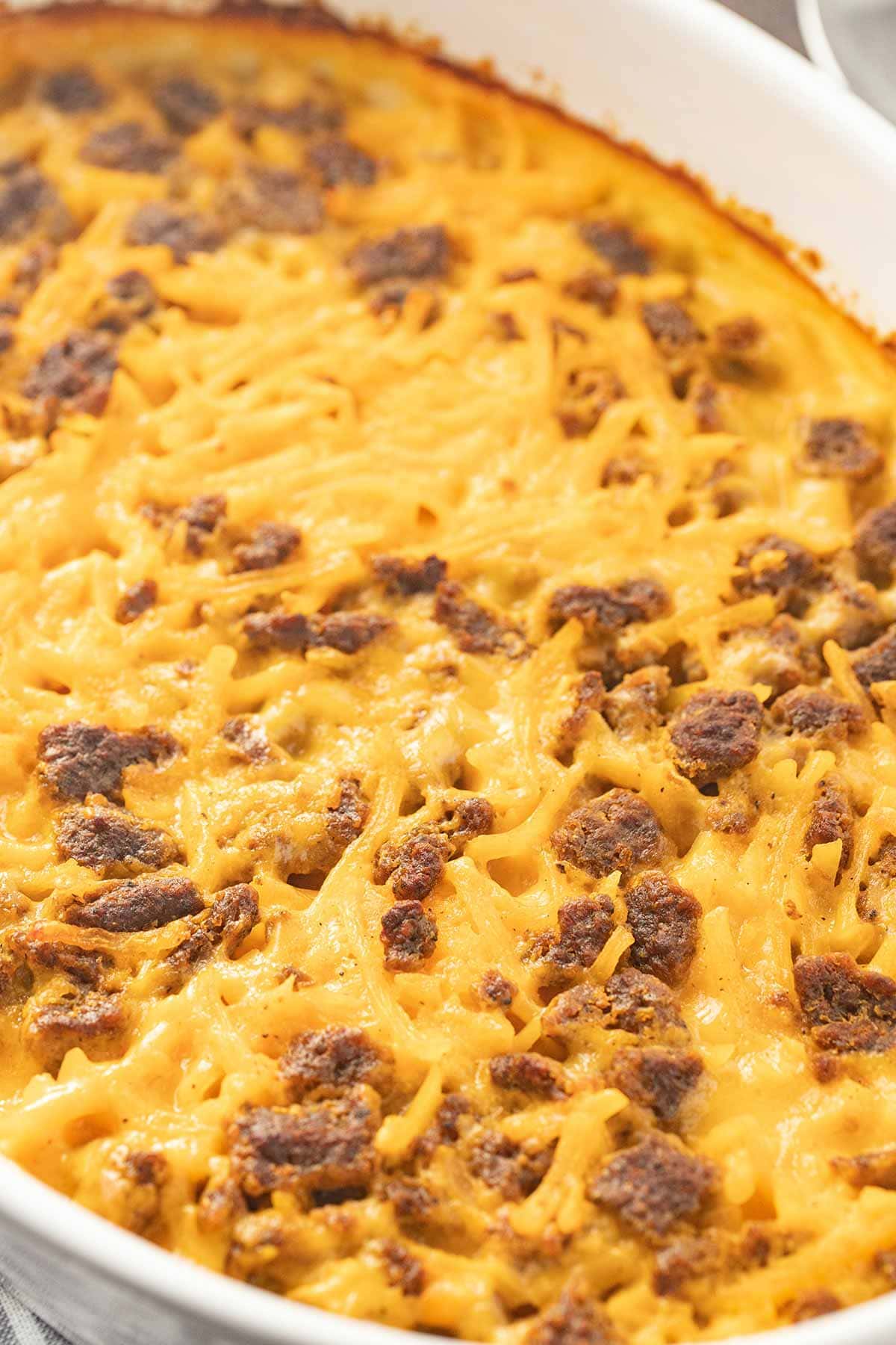 Close up of Potato Cheese Sausage Casserole, showing sausage bits and cheesy top, in white oval baking dish.