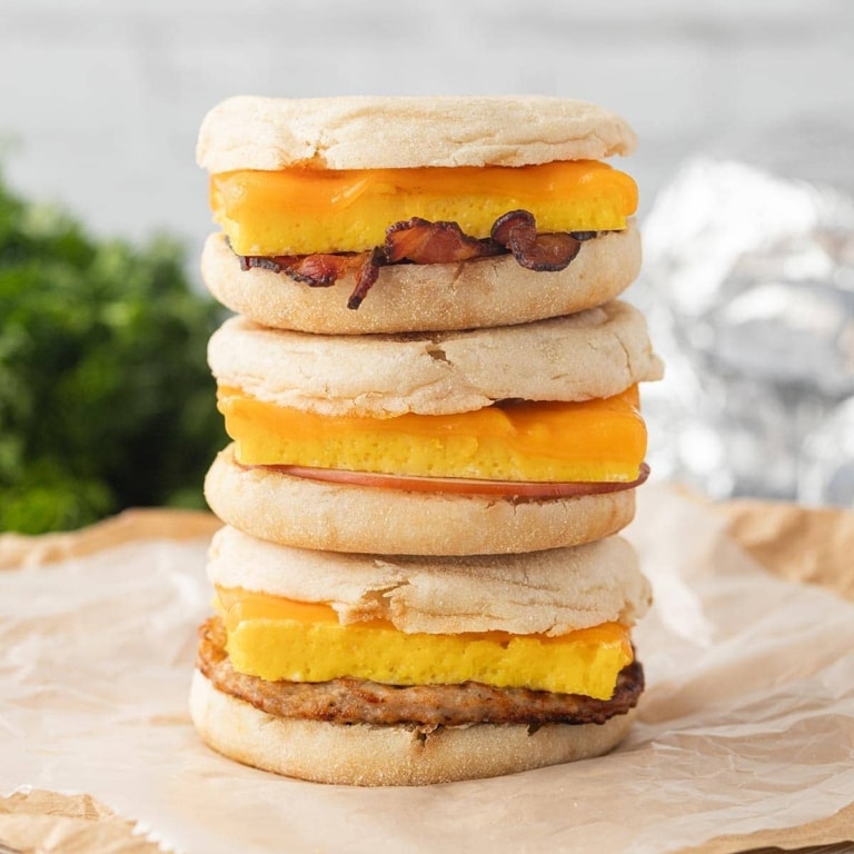 A stack of three Freezer Breakfast Sandwiches on parchment paper, showing the various layers and meat options.