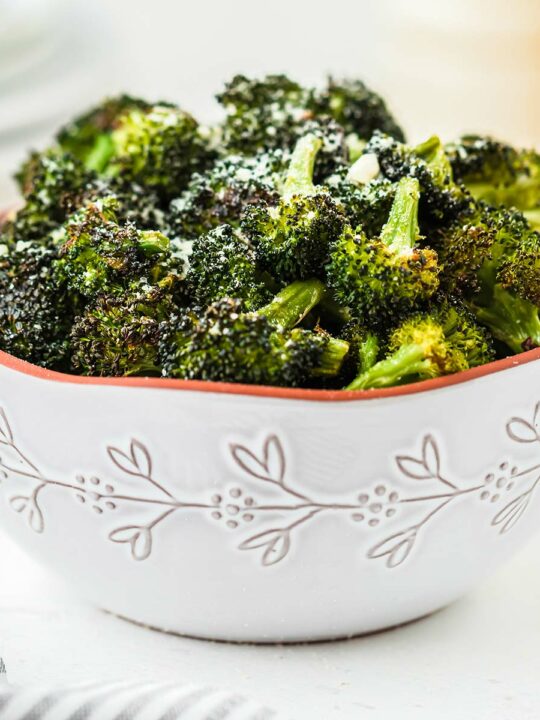 A bowl of roasted broccoli, garnished with grated Parmesan cheese.