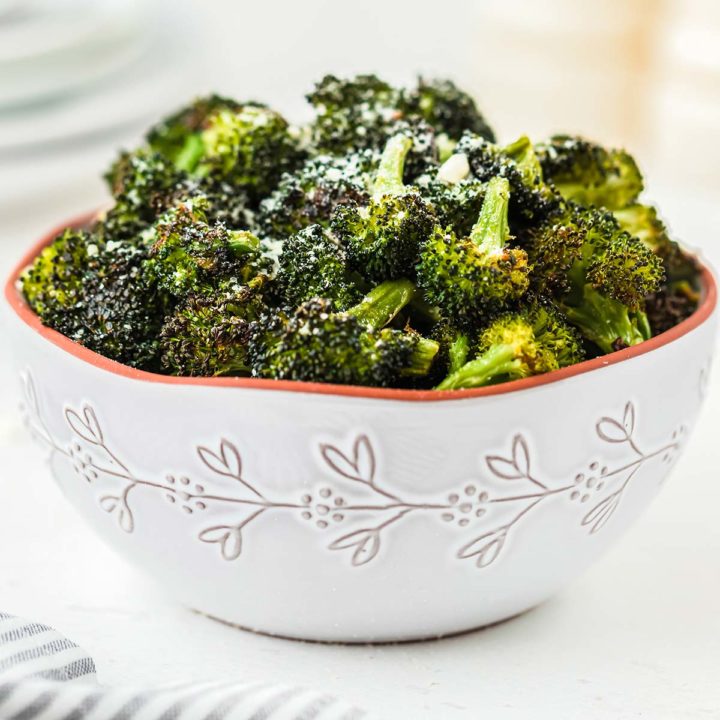 A bowl of roasted broccoli, garnished with grated Parmesan cheese.