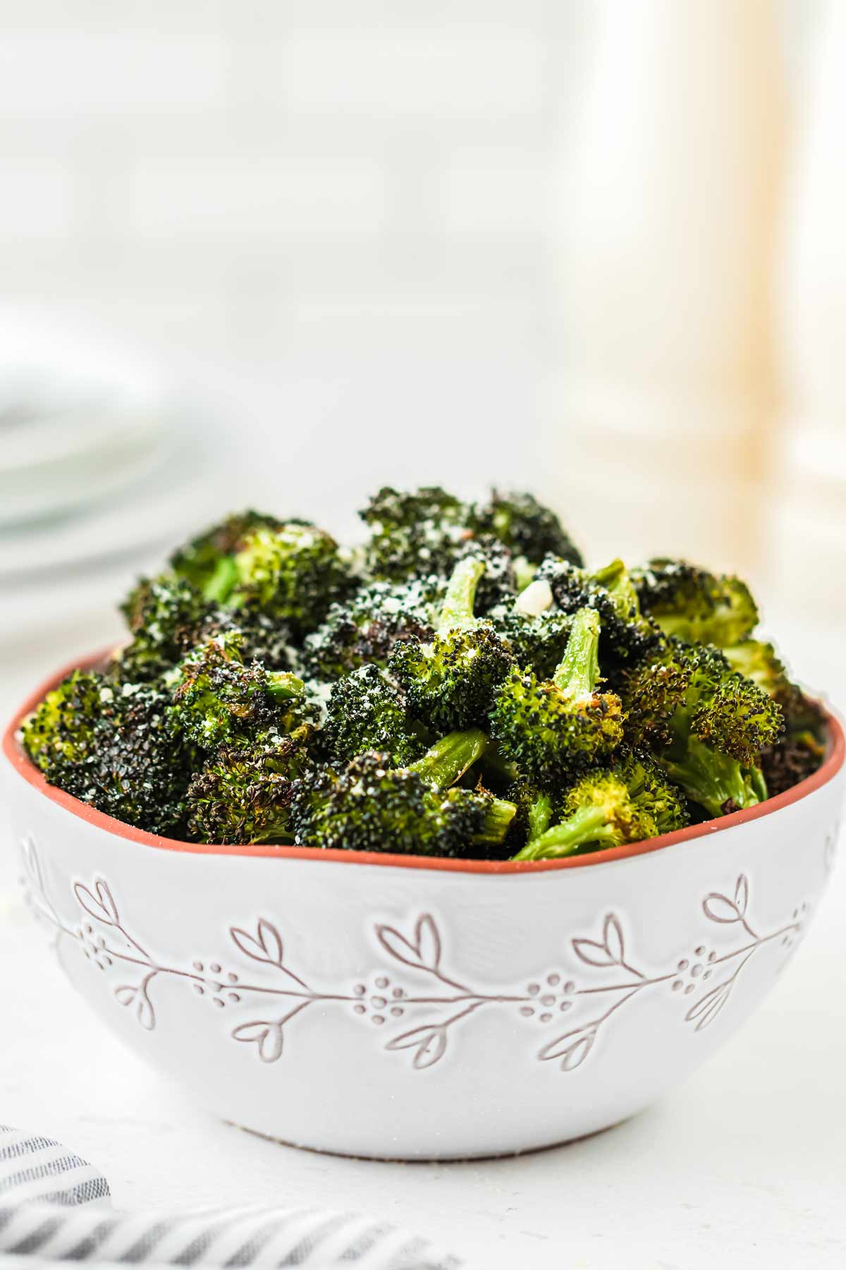 Roasted broccoli in a light gray bowl on a countertop, garnished with grated Parmesan cheese.