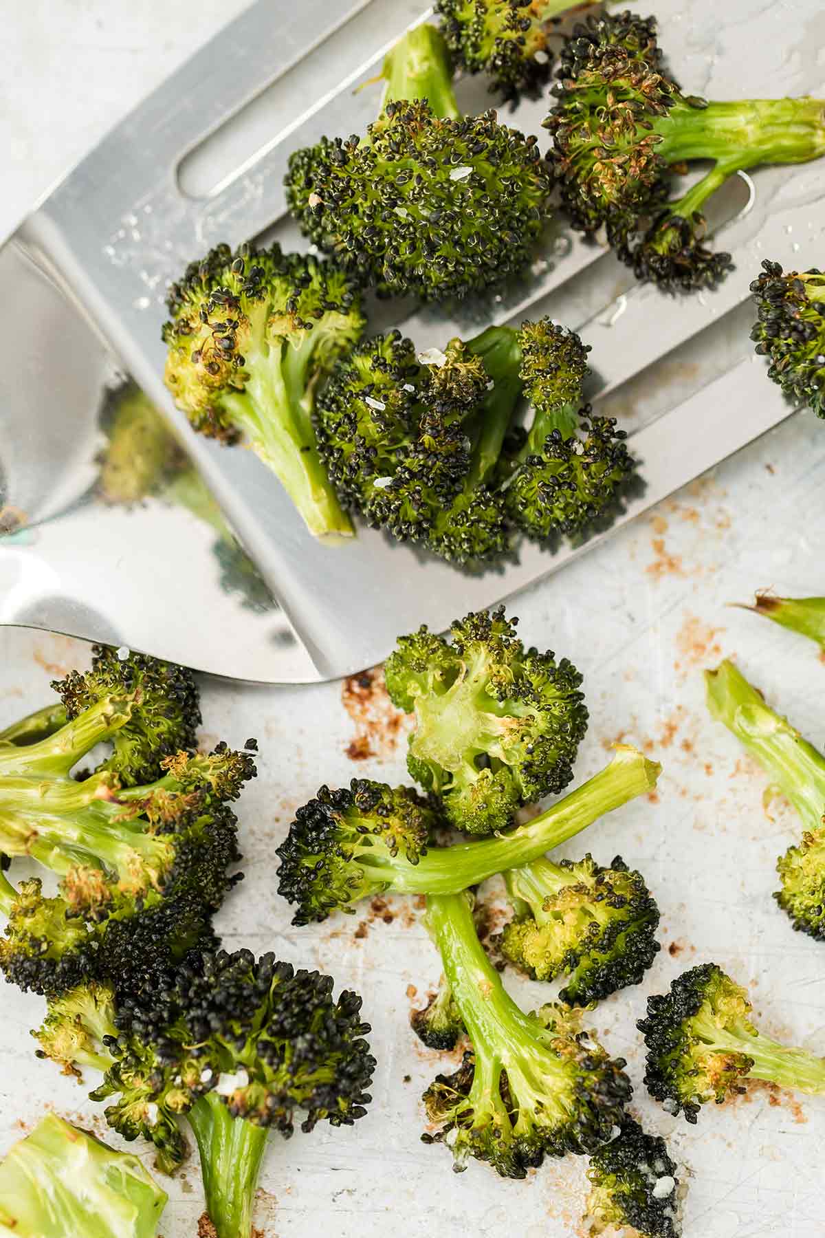 Close up overhead shot of roasted broccoli on a baking sheet with a silver spatula.