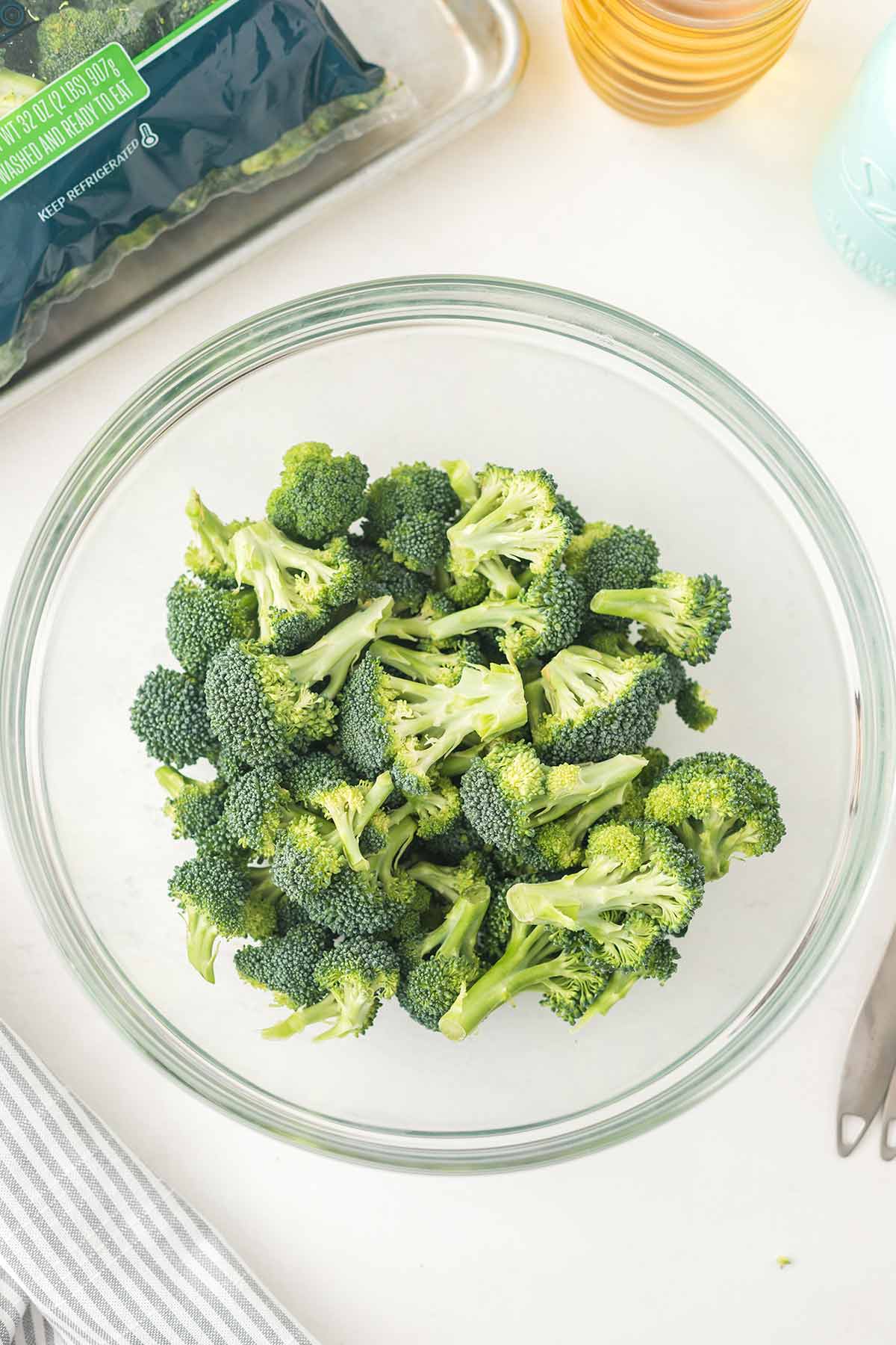 Overhead shot of broccoli florets in glass mixing bowl on tabletop.