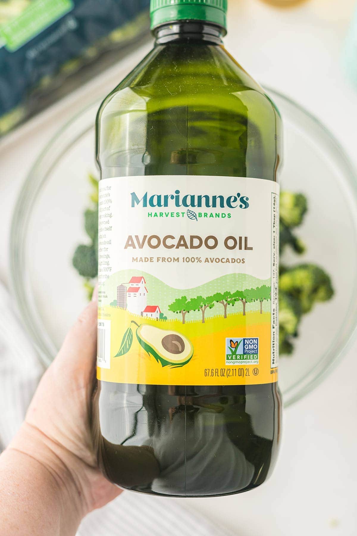 Overhead shot of bottle of avocado oil held above bowl of broccoli.