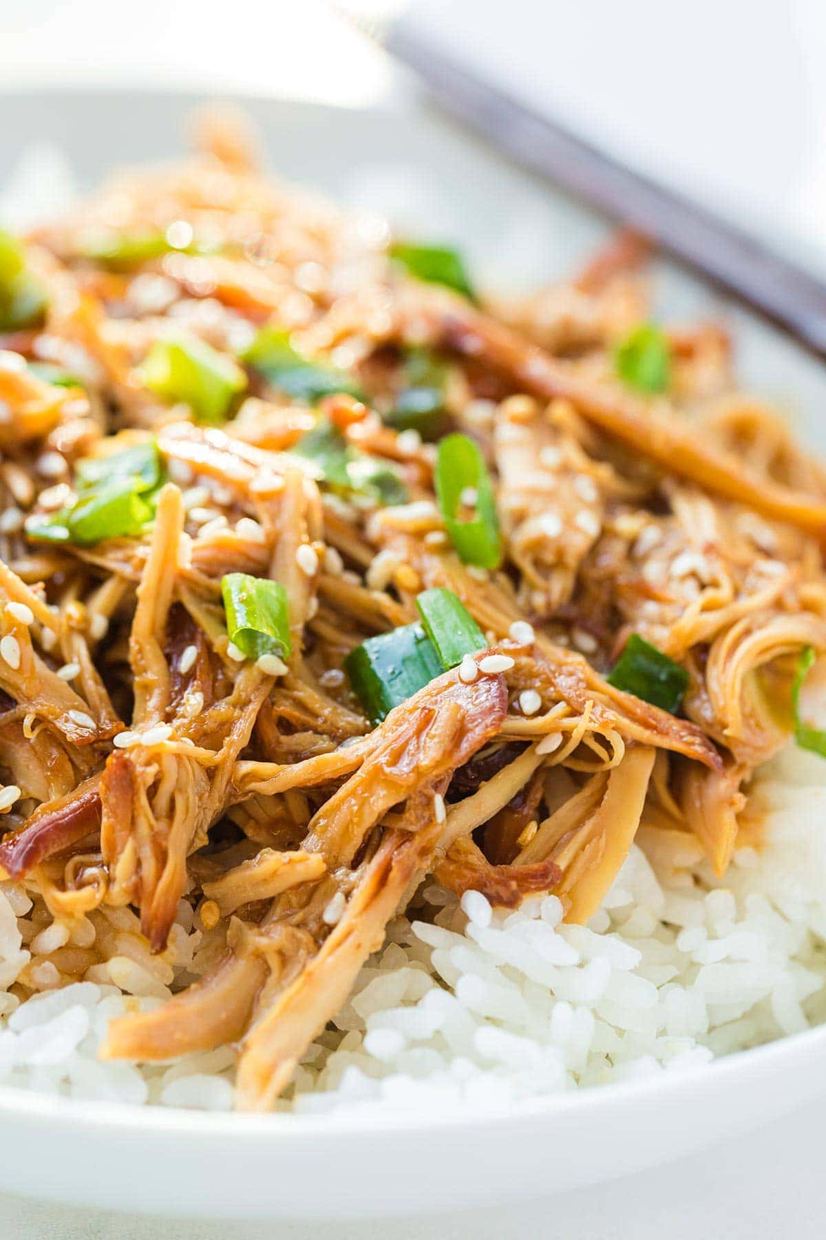 Closeup shot of easy crock pot honey sesame chicken freezer meal cooked and served on a bed of white rice, garnished with toasted sesame seeds and sliced green onion.